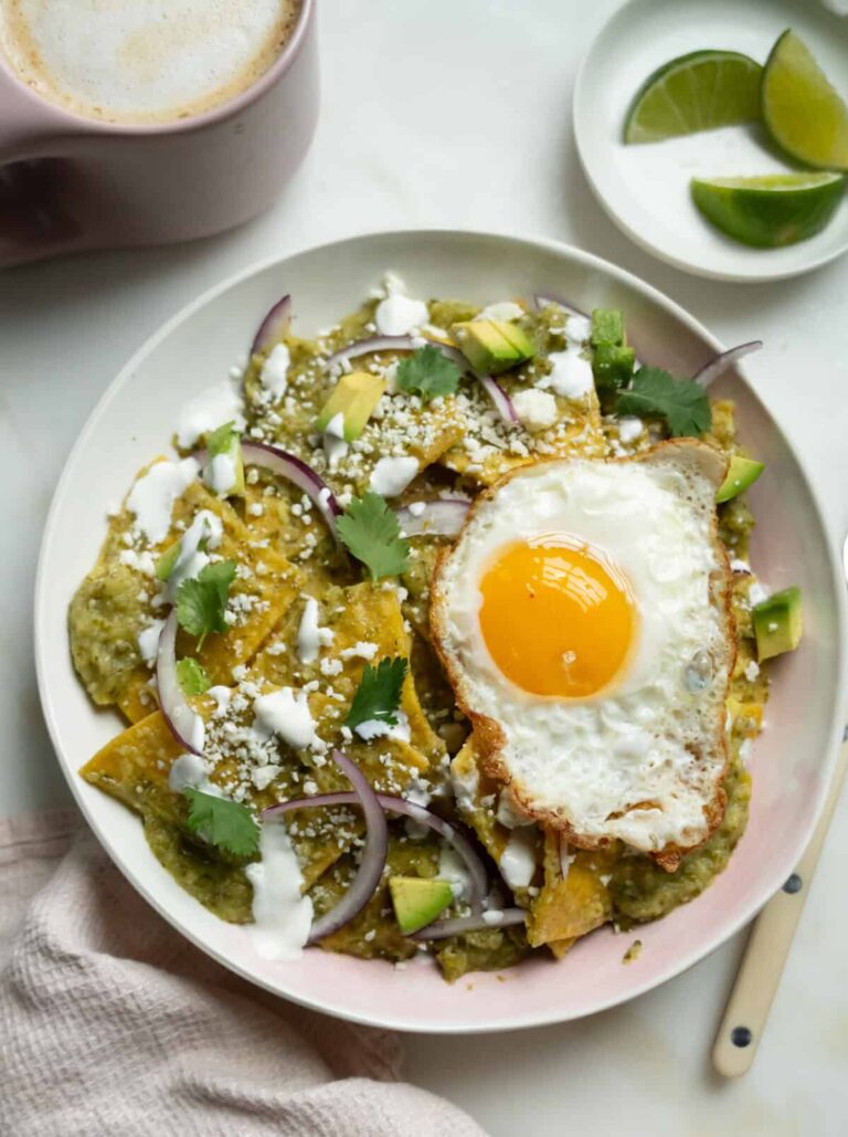 चीलक्वाइल्स शीर्ष पर एक तले हुए अंडे के साथ एक कटोरे में वर्क्स। एक कप कॉफी के साथ किनारे पर नीबू।