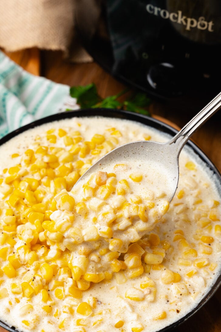 क्रीमयुक्त मकई के एक स्कूप के साथ चांदी का चम्मच जिसे क्रॉक पॉट में पकाया गया है।