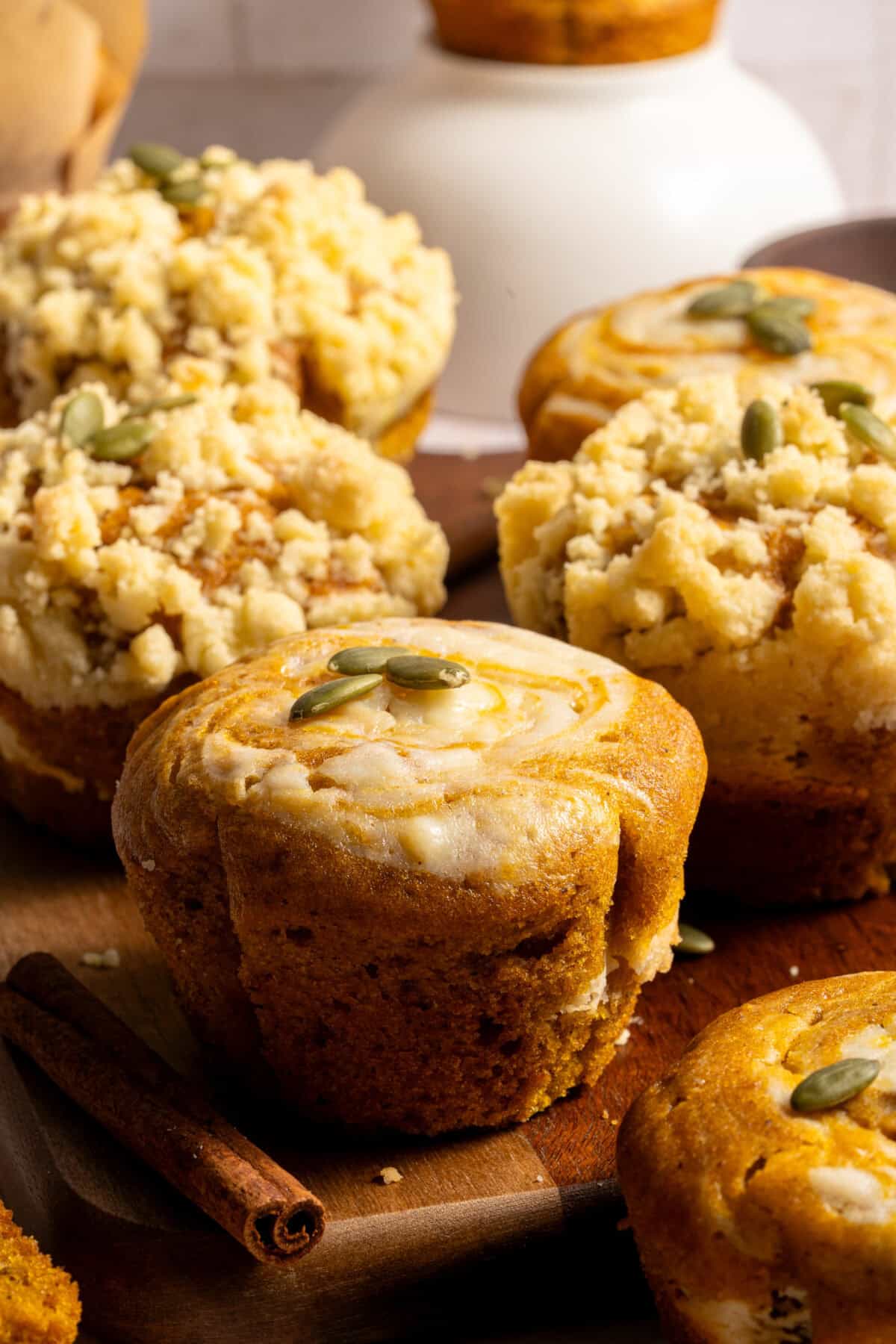 कटिंग बोर्ड पर कद्दू क्रीम चीज़ मफिन, ऊपर कद्दू के बीज।