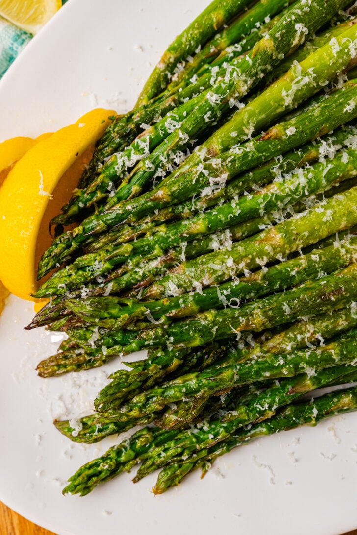 सफेद प्लेट में भुने हुए शतावरी के ऊपर कसा हुआ परमेसन चीज़ और नींबू डालें।