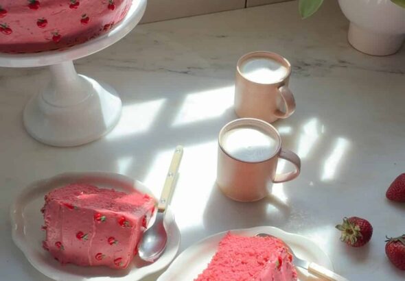 स्ट्रॉबेरी लेयर केक स्लाइस, केक स्टैंड पर केक, और कॉफी के कप।