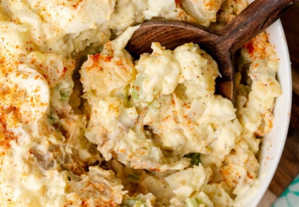 तीखी सरसों और कड़े उबले अंडे के साथ, यह दक्षिणी आलू सलाद पारिवारिक समारोहों के लिए एकदम आसान साइड डिश है और छुट्टियों के जश्न के लिए जरूरी है। आलू का सलाद लकड़ी के चम्मच से कटोरे से निकाला गया।