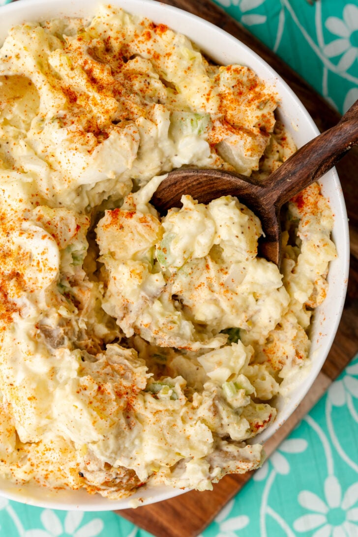 तीखी सरसों और कड़े उबले अंडे के साथ, यह दक्षिणी आलू सलाद पारिवारिक समारोहों के लिए एकदम आसान साइड डिश है और छुट्टियों के जश्न के लिए जरूरी है। आलू का सलाद लकड़ी के चम्मच से कटोरे से निकाला गया।